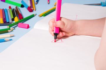 a small child draws with a pink felt-tip pen a heart in an album, copy space, top view, blue background, what to do with a quarantined child, activities for children at home