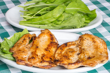 grilled chicken breast with arugula salad on top of checkered tablecloth
