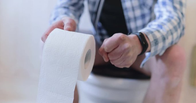 Man suffers constipation on lavatory pan with toilet paper roll in hand