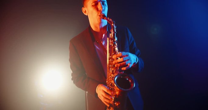 Cool saxophone player performing a solo on stage, spotted by red and blue light. Musician playing in jazz band - close up 4k footage