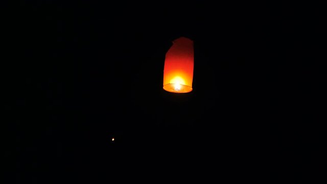 People launching a Chinese sky fly fire lantern in the night sky to make a wish during festival.
