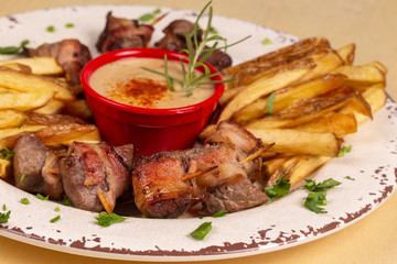 portion of meat skewer with bacon and french fries served with sauce