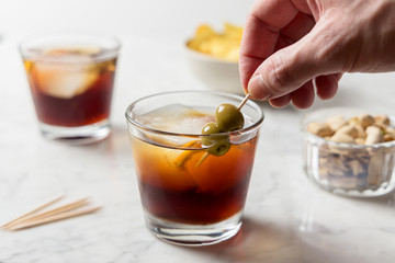 Man's hand picking olives from red vermouth