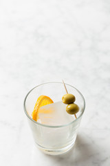 Orange slice, olives and a big ice cube inside a glass. Vermouth preparation