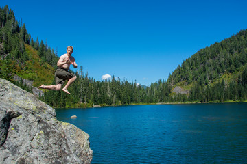Adventurous male hiker jumping into an alpine lake in Washington State.
