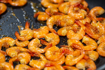 close up shrimp frying with garlic in olive oil in black pan.