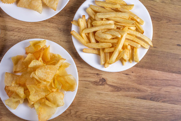 portion of potato chips and french top view on wooden background