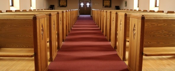 Looking down long aisle toward the front doors with light coming through the glass crosses in empty church