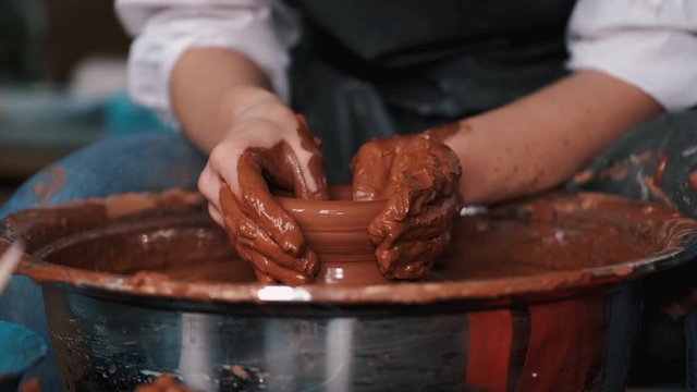 Artist works in creative studio. Person uses pottery wheel. Woman's hands are anointed with clay.