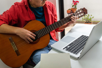 Obraz premium Portrait of a man taking classic guitar lessons online in a room at home during quarantine