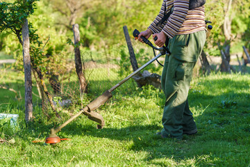Midsection of unknown Young caucasian man farmer gardener standing in the field with string trimmer petrol Brushcutter ready to cut weed grass working on the farm cutting in the field in sunny day