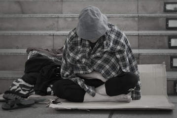 Homeless man sitting on the street in the shadow of the building. He begging for  help and money....