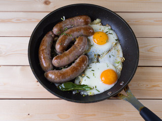 Homemade delicious sausages and fried eggs in a pan on a wooden surface