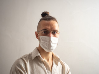 Young Blond Hair Caucasian Male in White Shirt and Glasses Wearing a Disposable Face Mask for Covid-19, Cought, Flu, Virus, Viral Protection is Looking at the Camera