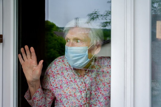 Personne &acirc;g&eacute;e avec masque chirurgical, regardant par la fen&ecirc;tre