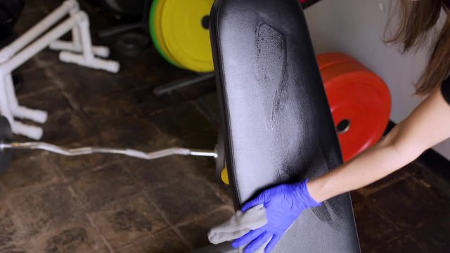 Woman cleaning and sanitizing a workout bench at a gym because of the reopening during the coronavirus pandemic