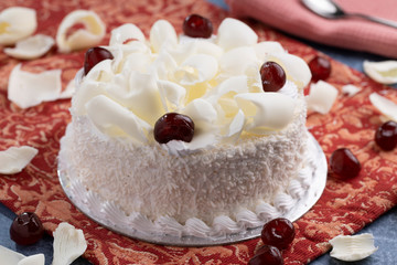 White forest cake with grated white chocolate and glazed cherry topping