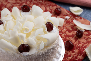 White forest cake with grated white chocolate and glazed cherry topping