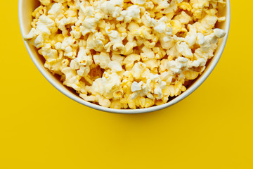 Popcorn in a bowl on yellow background, top view. Entetainement concept.