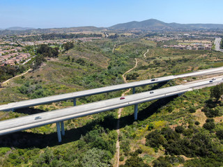 Naklejka premium Aerial view of road highway bridge, viaduct supports in the valley among the green hills, transport infrastructure. California, USA 