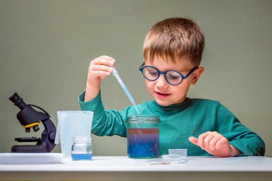 Small boy studies chemistry. Testing tubes with liquid for research. Learn for future. Biology science. Preschooler at home. Little genius child. Pupil using microscope. Young confident scientist