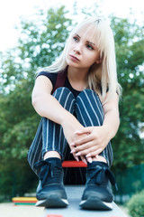 Sad beautiful blonde girl on seesaw in park and thinks about her problem. Bygone childhood concept.