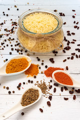 Ingredients for cooking pilaf: rice in a glass dish in the background, garlic in the front, cumin, saffron and paprika in spoons, barberry and black pepper are scattered on the table.