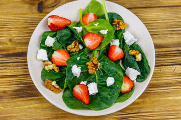 Fresh healthy salad with strawberry, spinach, walnuts and feta cheese on wooden table. Top view