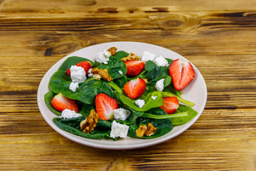 Fresh healthy salad with strawberry, spinach, walnuts and feta cheese on wooden table