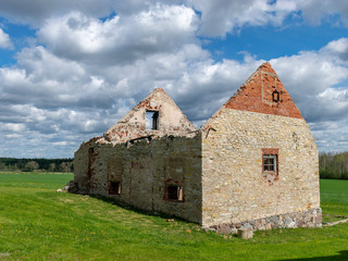 the ruins of an old building in a green field, white cumulus clouds cover the sky