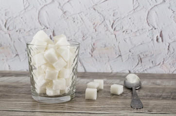 A glass of sugar crystals or cubes on a wooden table. Intake of bad calories.
