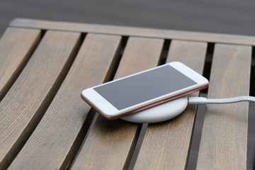 close up one smartphone on wireless charger on wooden table. blur background