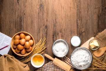 Pictures of ingredients for making cakes bakery around, such as eggs, flour, sugar, butter, recipe book and equipment for making on a wooden floor, with copy space.