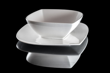 Square white empty plate for dinner on dark background. Dishes isolated on black. Restaurant kitchen minimalistic concept.