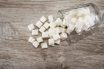 A glass of sugar crystals or cubes on a wooden table. Intake of bad calories.