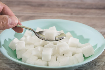 Fototapeta na wymiar sugar cubes in a plate and spoon on a wooden background. Sugar harm concept. Eat sugar with a spoon.