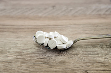 Fototapeta na wymiar Pills in a spoon on a wooden background.
