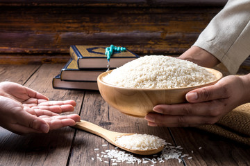 Hands holding a wooden bowl of rice grains for zakat, Islamic zakat concept. Muslims to help the...