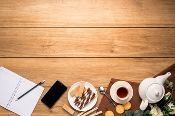 Afternoon tea set with bread, crackers, Wafer, and a mobile phone and a notebook beside on the wooden table, with copy space, top view.