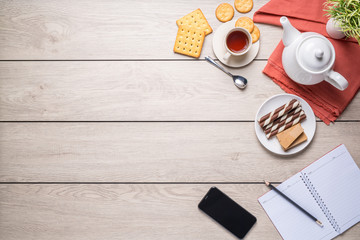 Afternoon tea set with bread, crackers, Wafer, and a mobile phone and a notebook beside on the wooden table, with copy space, top view.