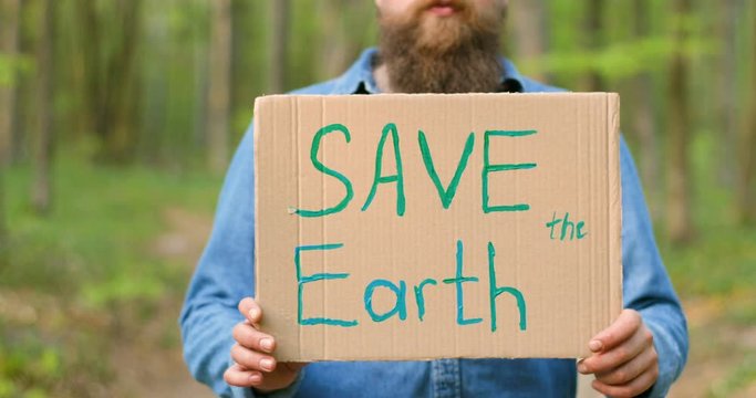 Close up of carton poster with words Save the Earth in hands of Caucasian man. Male eco activist standing in forest or park on sunny day with single protest.