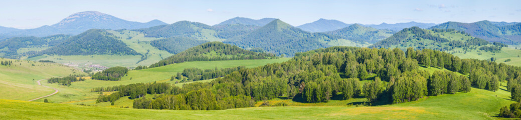 Panoramic mountain view. Bright sunlight, spring greens of forests and meadows.