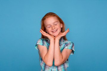Emotional portrait of a young funny naughty girl with red hair  against  blue background