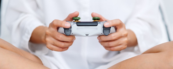 Closeup image of a woman holding game controller while playing games , sitting on a white cozy bed...