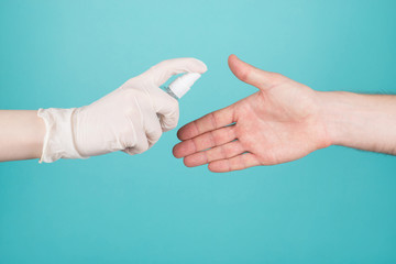 Stop spreading coronavirus patient concept. Cropped close-up photo of woman in gloves sprays sanitizer on man's hand isolated on blue teal turquoise background