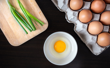 closeup spring onion on wood butcher and fresh chicken egg in bowl and group of egg in box on wooden kitchen table for healthly and delicious meal or food cook concept