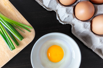 closeup spring onion on wood butcher and fresh chicken egg in bowl and group of egg in box on wooden kitchen table for healthly and delicious meal or food cook concept