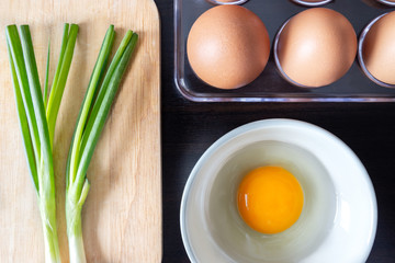 closeup spring onion on wood butcher and fresh chicken egg in bowl and group of egg in box on wooden kitchen table for healthly and delicious meal or food cook concept
