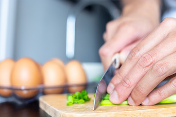 Obraz na płótnie Canvas closeup of people hand and knife slice spring onion on wood butcher and fresh chicken egg in bowl and group of egg in box on wooden kitchen table for healthy and delicious meal or food dinner cook