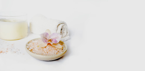Pink Himalayan rock salt in a bowl with an orchid on top in the foreground and a candle and towel in the background